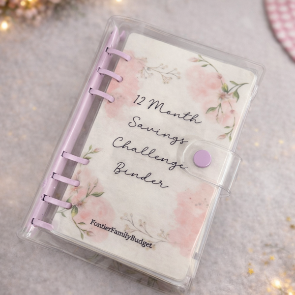 12 Month Savings Challenge Binder with floral design on a gray surface with decorative lights.