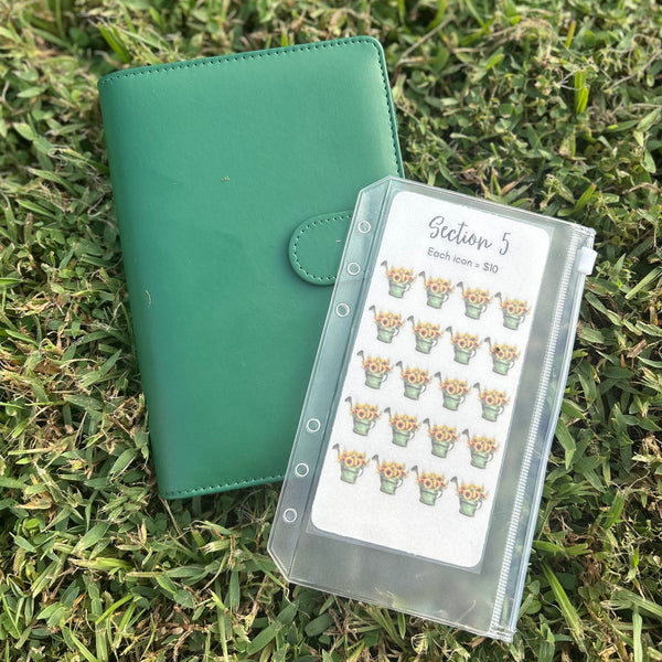 Green planner with a clear case containing stickers on grass