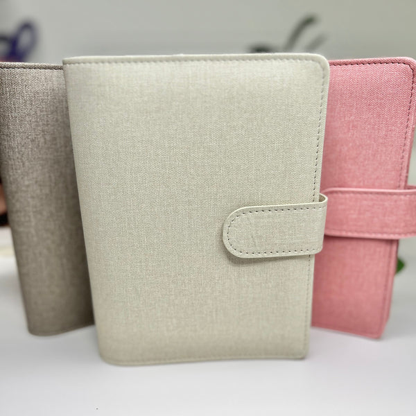 Three fabric-bound books in beige, gray, and pink on a white surface.