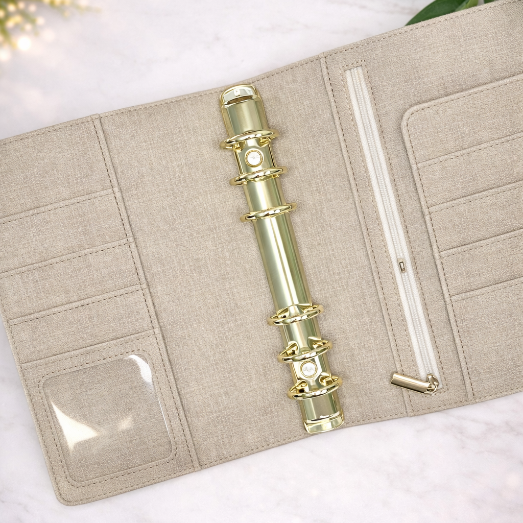 Beige planner with gold ring binding on a white surface with green leaves in the background