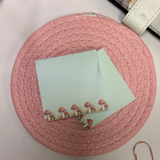 Round pink woven coaster with a card featuring mushroom illustrations on a light surface.