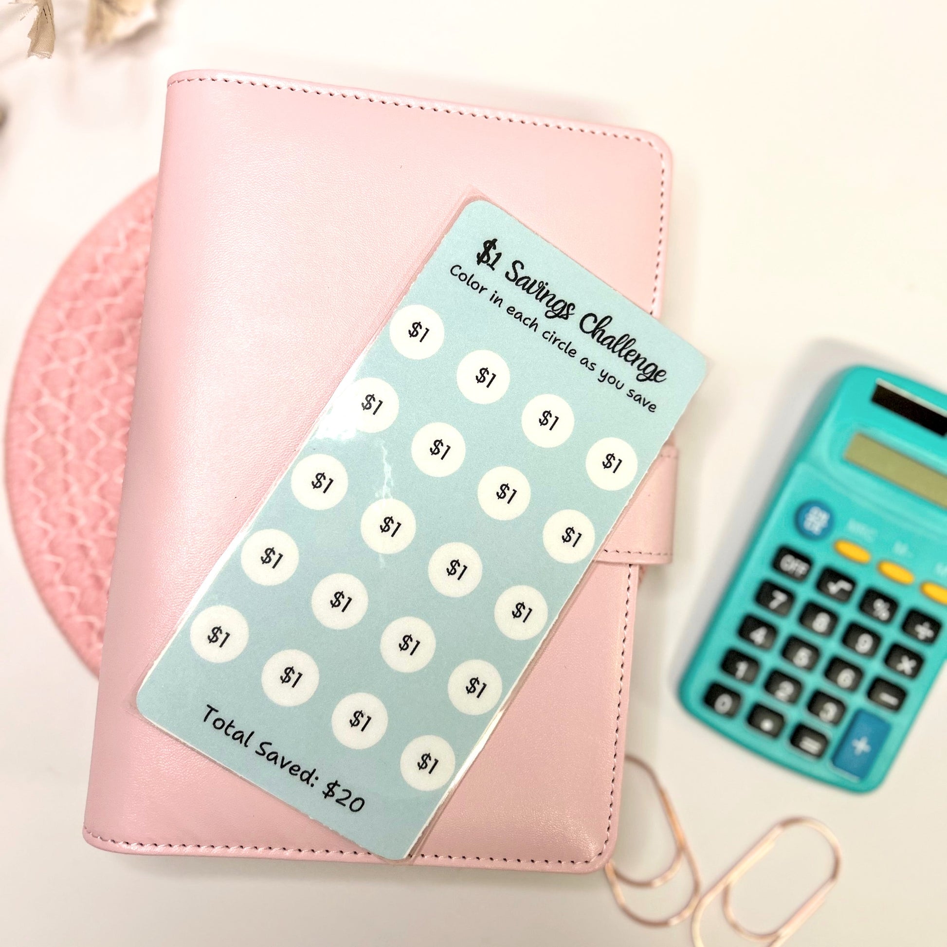 Pink planner with a savings challenge tracker and teal calculator on a light background