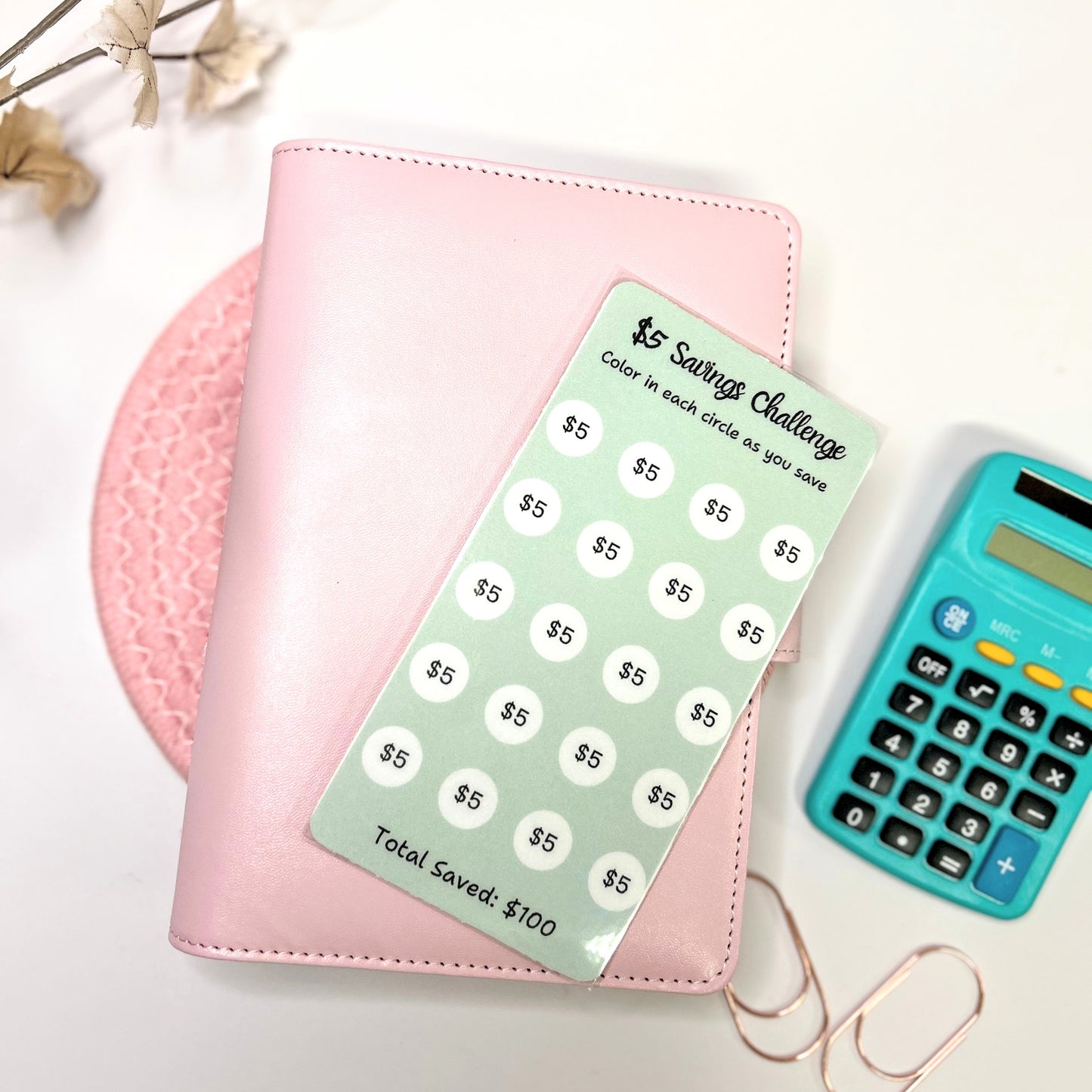 Pink planner with a green savings challenge tracker and a blue calculator on a light background