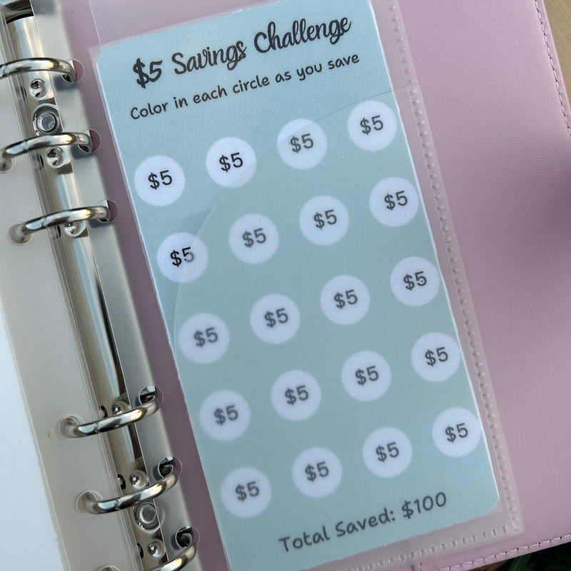 Pink planner with a savings challenge tracker on a wooden surface
