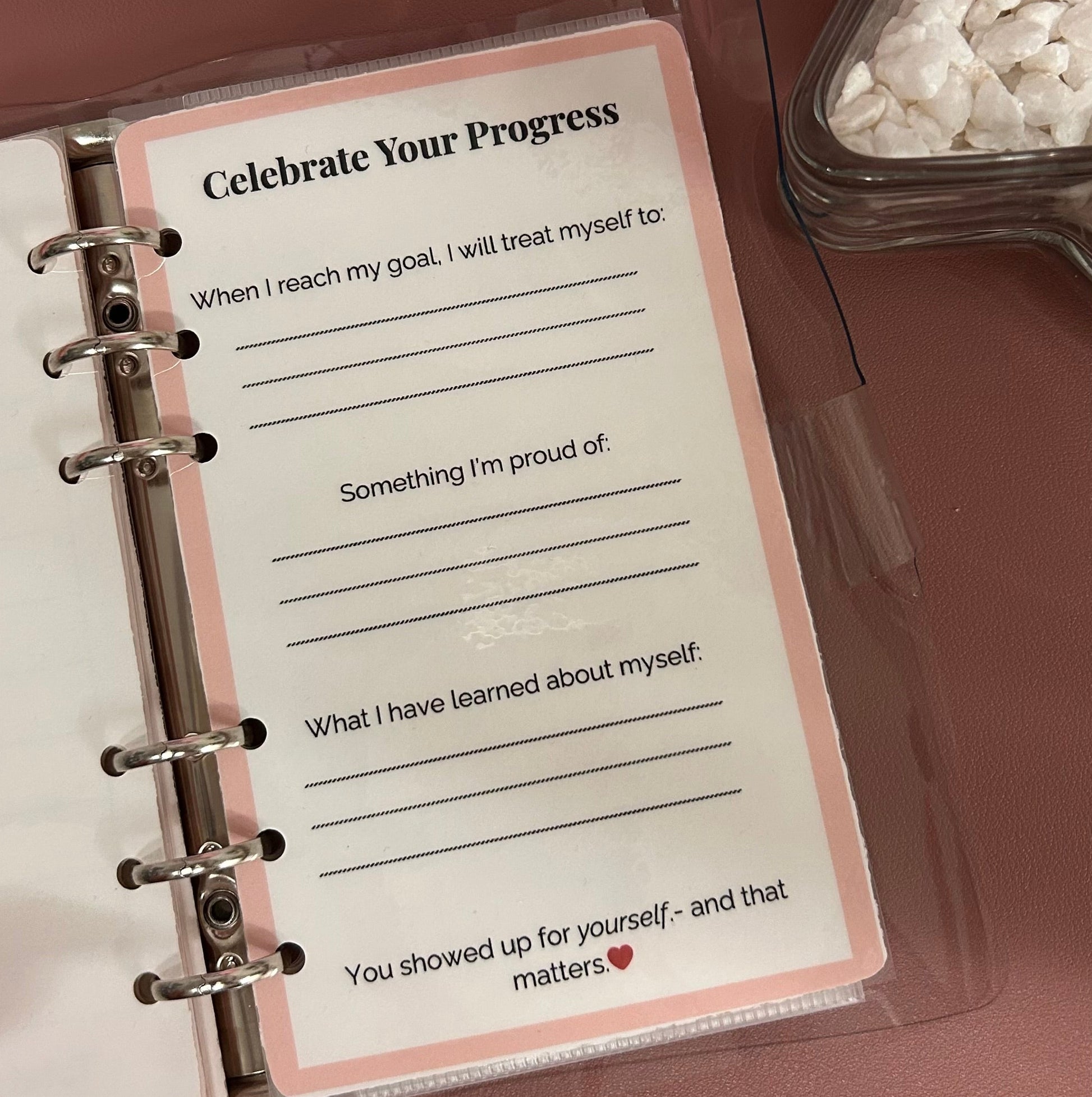 Notebook with a motivational card titled 'Celebrate Your Progress' on a wooden surface.