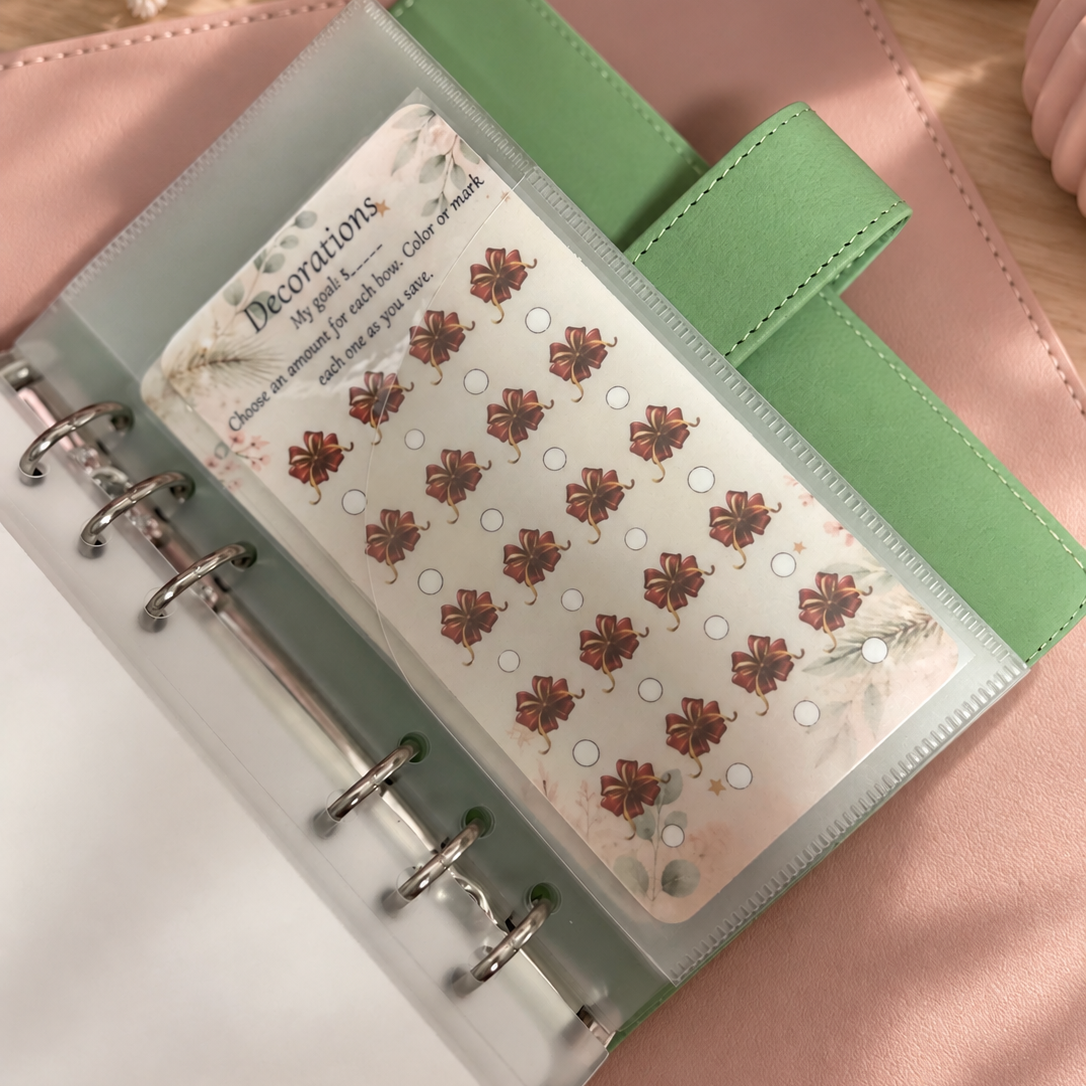 A close-up of a clear plastic binder ring set holding a decorative sticker sheet. The sheet features a repeating pattern of red and brown floral motifs with small white circles, photographed against a soft pink textured background.