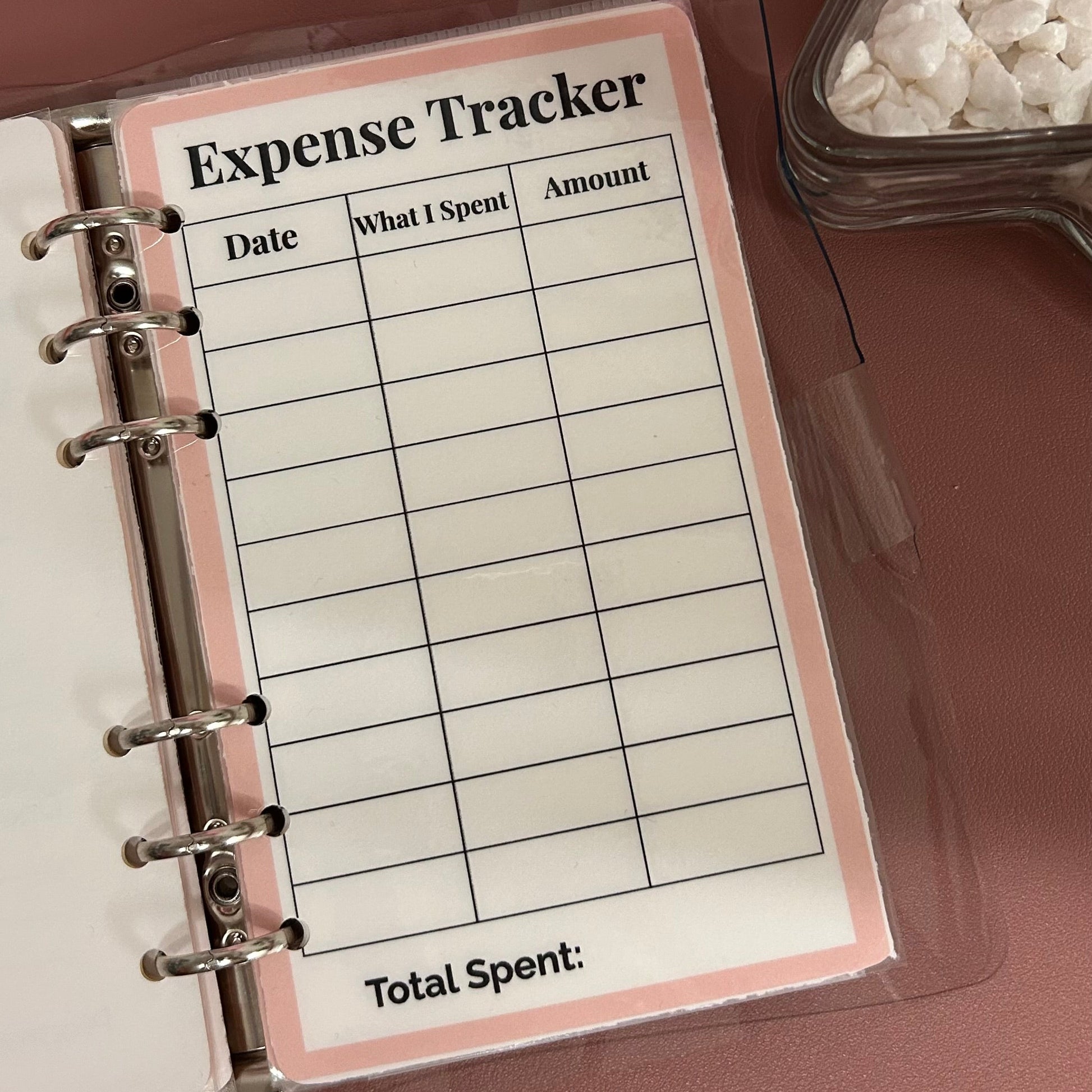 Expense tracker page in a planner with a pink border on a brown surface.