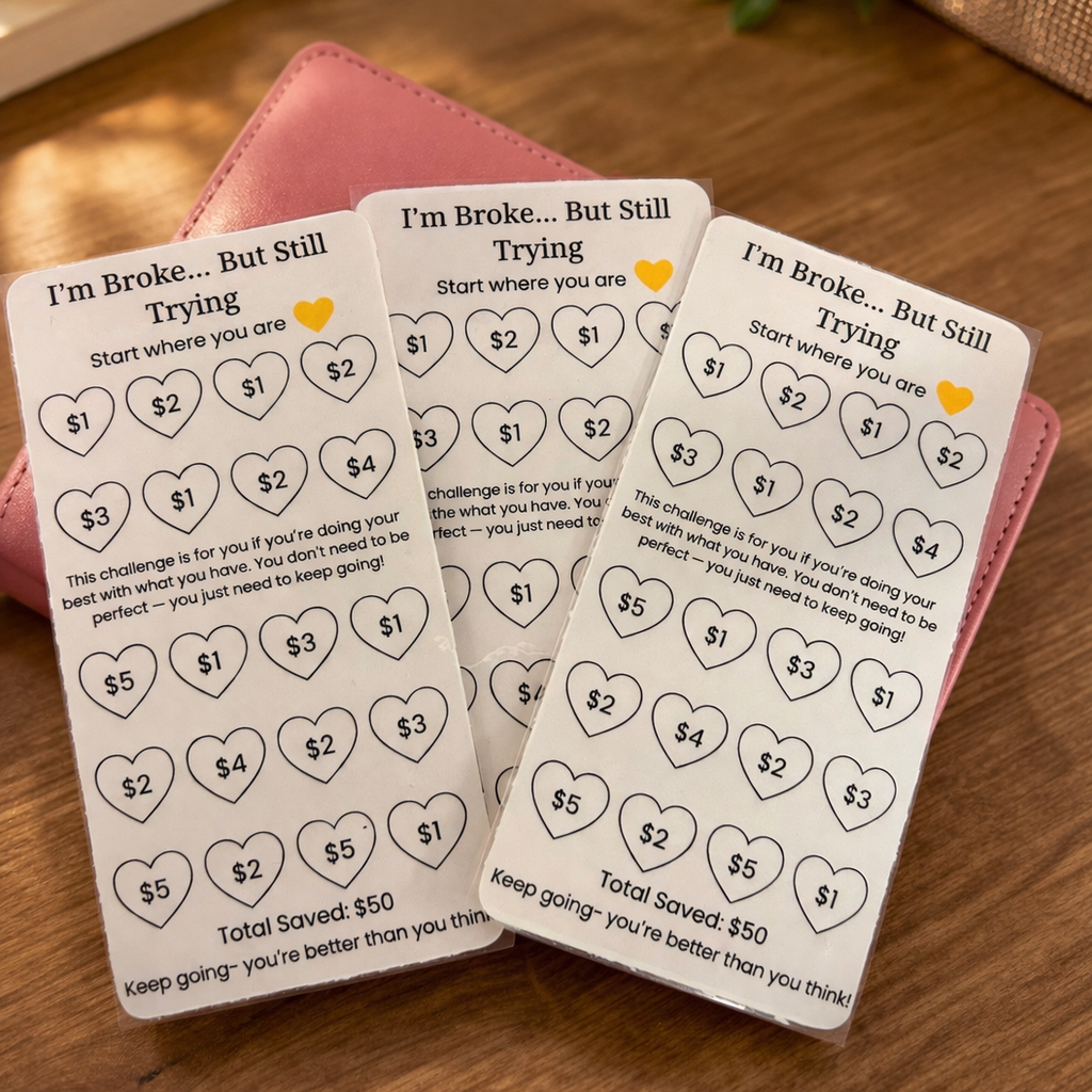 Three 'I'm Broke... But Still Trying' saving challenge cards on a wooden surface with a pink wallet.