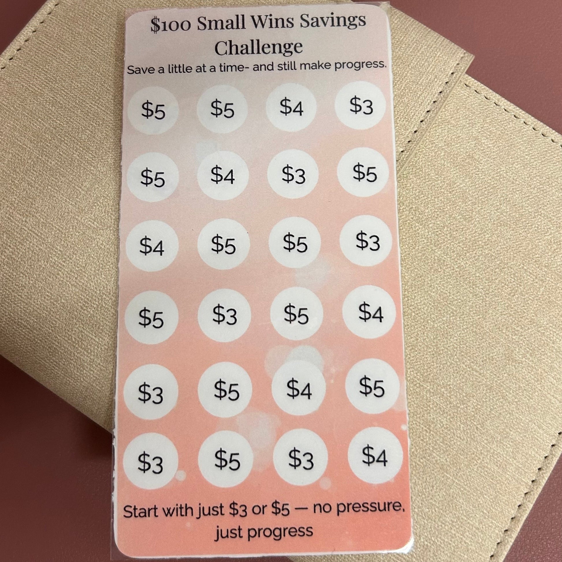 Small wins savings challenge card on a beige wallet with a brown background