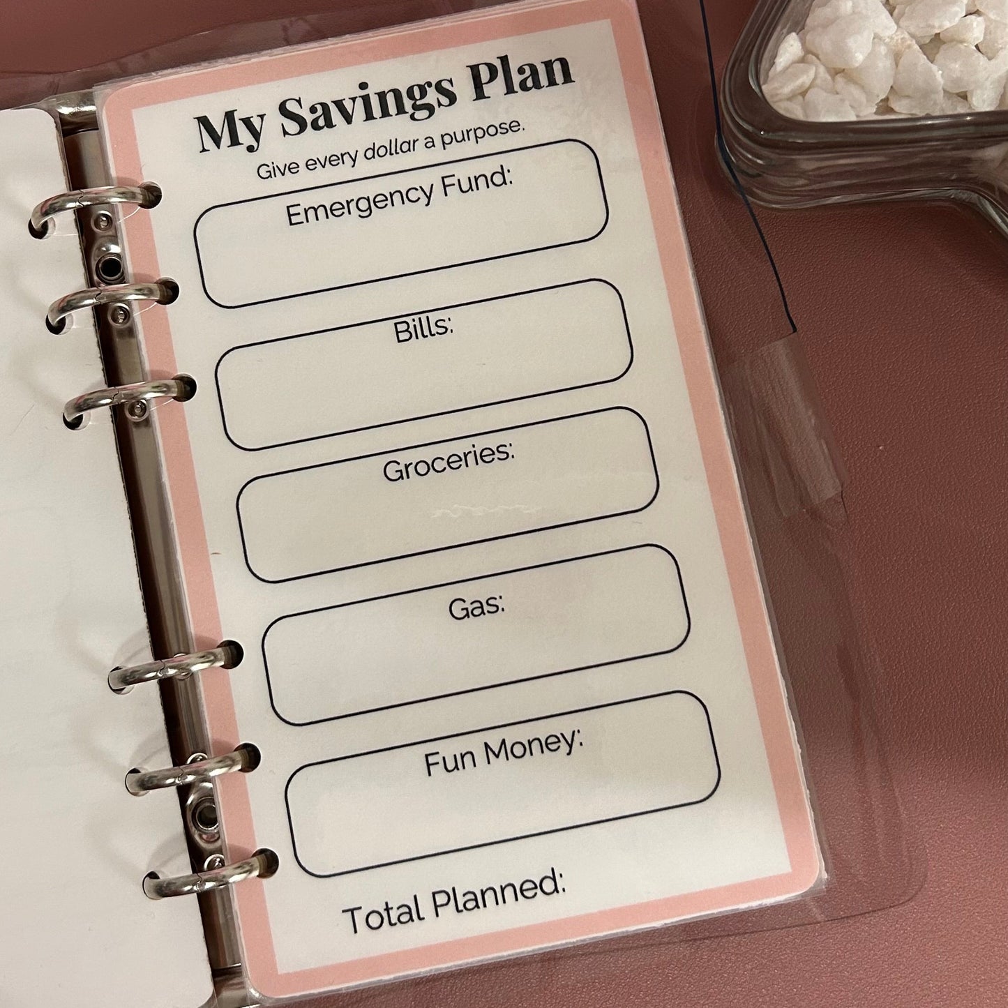 Savings plan worksheet in a planner with a pink cover on a brown surface.