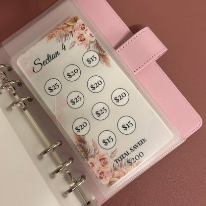 Pink planner with a clear plastic cover displaying money values on a pink background