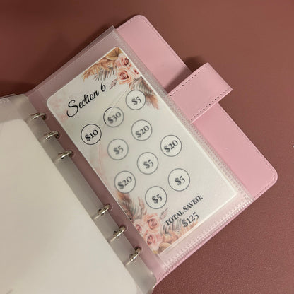 Pink planner with money clip attachment on a wooden surface