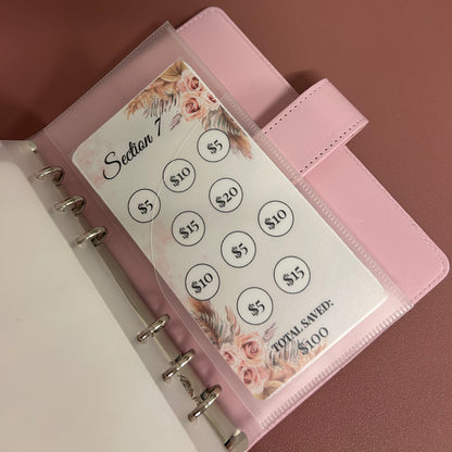 Pink planner with money clip attachment on a wooden surface