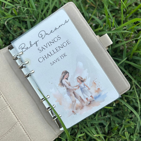 Notebook with 'Baby Dreams Savings Challenge' on a grass background
