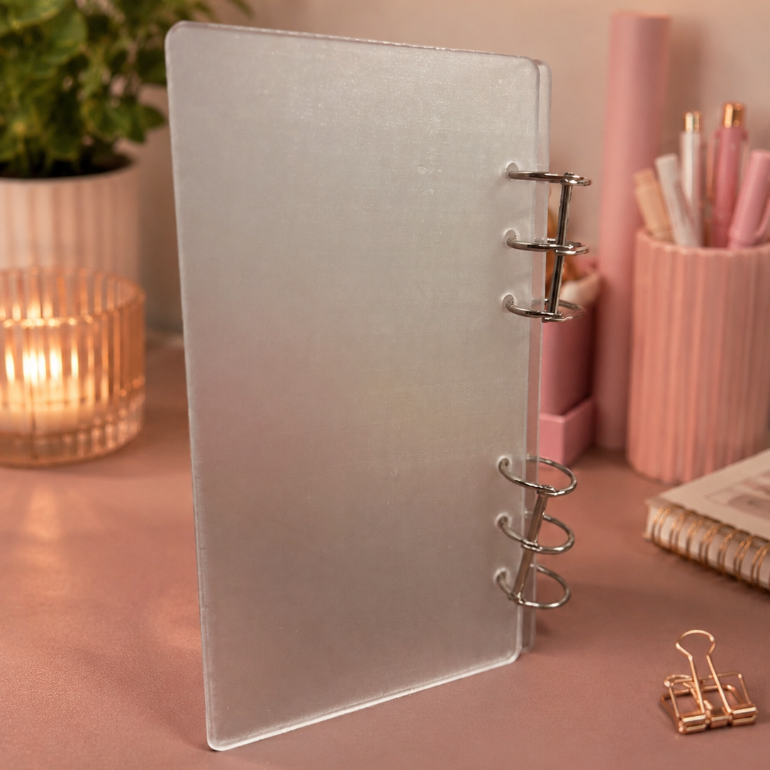 Silver spiral-bound notebook on a desk with stationery items and a plant in the background