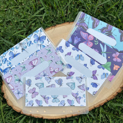 Set of butterfly-themed cash envelopes on a wooden block with grass background