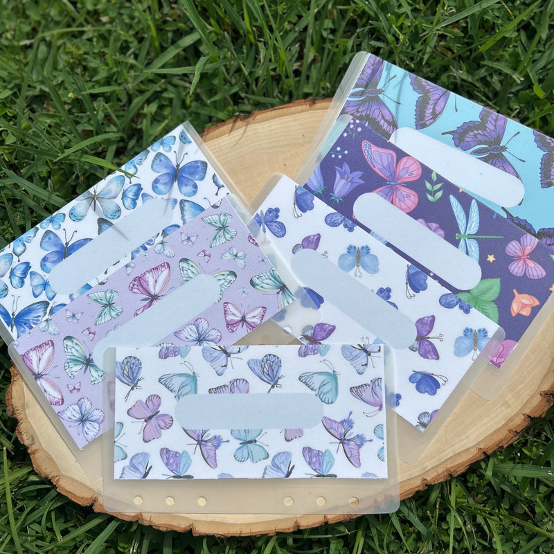 Set of butterfly-themed cash envelopes on a wooden block with grass background