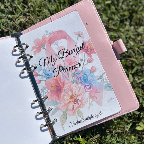 Pink budget planner with floral design on cover, held in grass