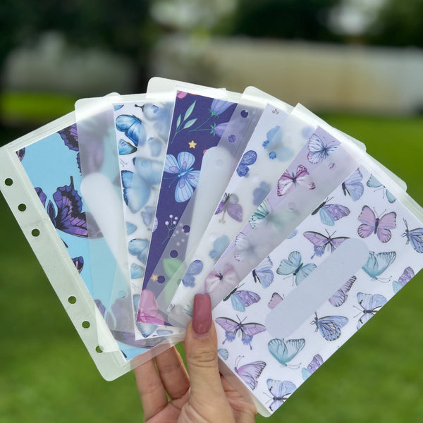 Hand holding colorful butterfly-themed cash envelopes with a blurred outdoor background