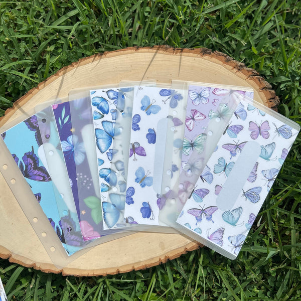 Set of butterfly-themed cash envelopes on a wooden stand with grass background
