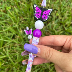 Decorative pen with butterfly design held by a hand on grass