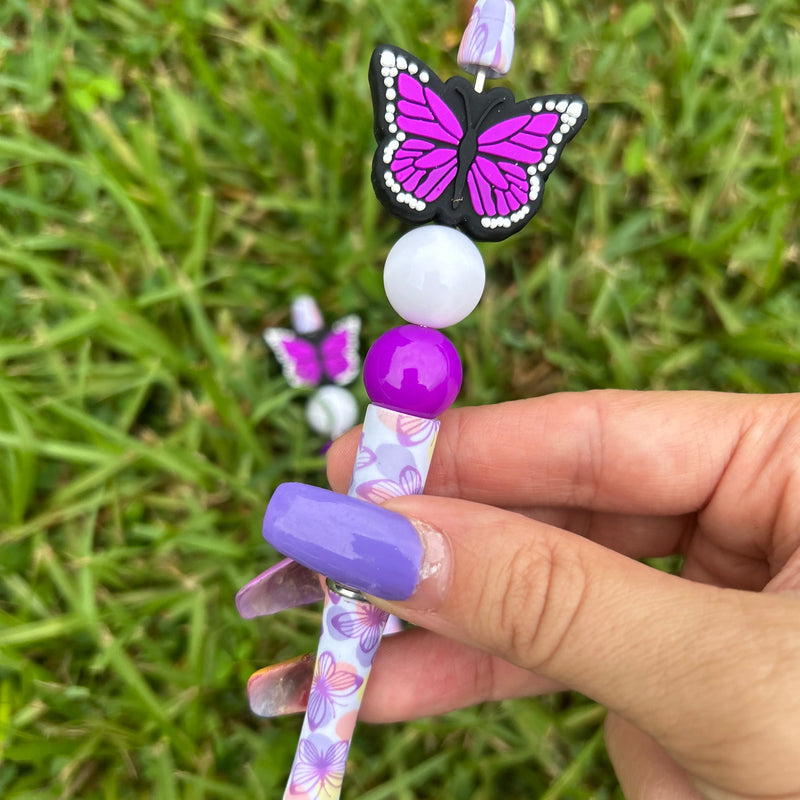 Decorative pen with butterfly design held by a hand on grass