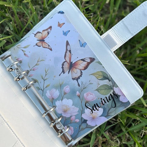 Notebook with butterfly design on the cover, placed on grass.