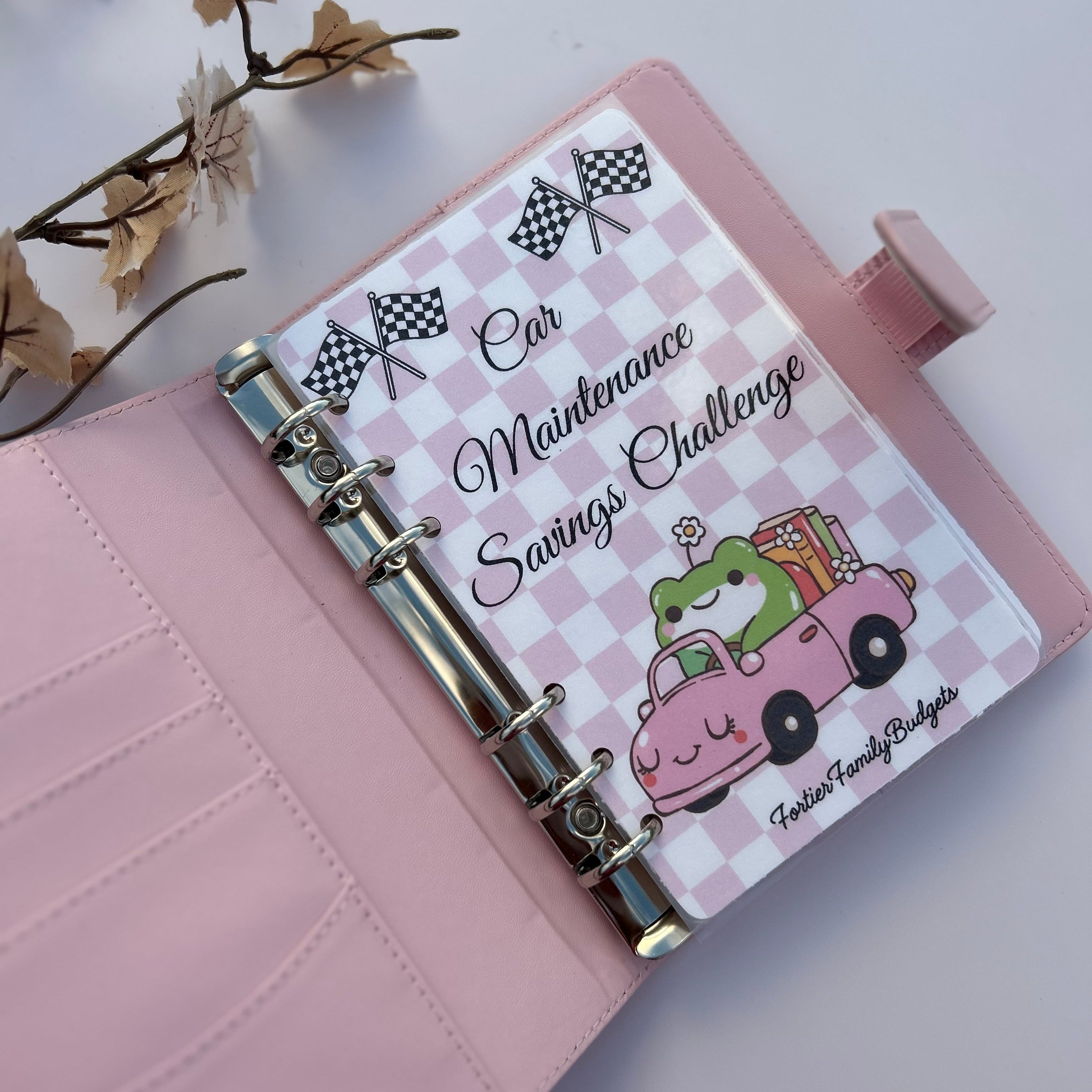 Pink planner with a car maintenance savings challenge design on a light gray background