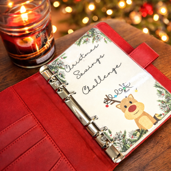 Red planner with Christmas-themed cover featuring a reindeer illustration, next to a lit candle on a wooden surface.