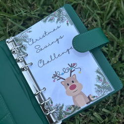 Green planner with a Christmas design on the cover, featuring a reindeer and text, placed on grass.