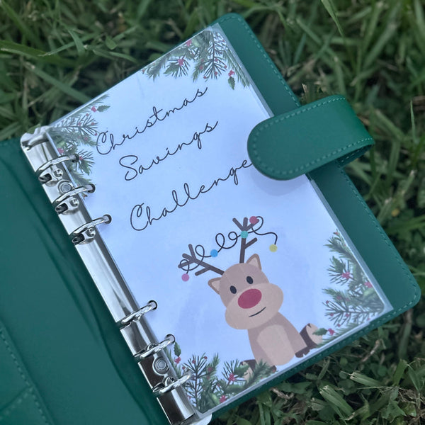 Green planner with a Christmas design on the cover, featuring a reindeer and text, placed on grass.