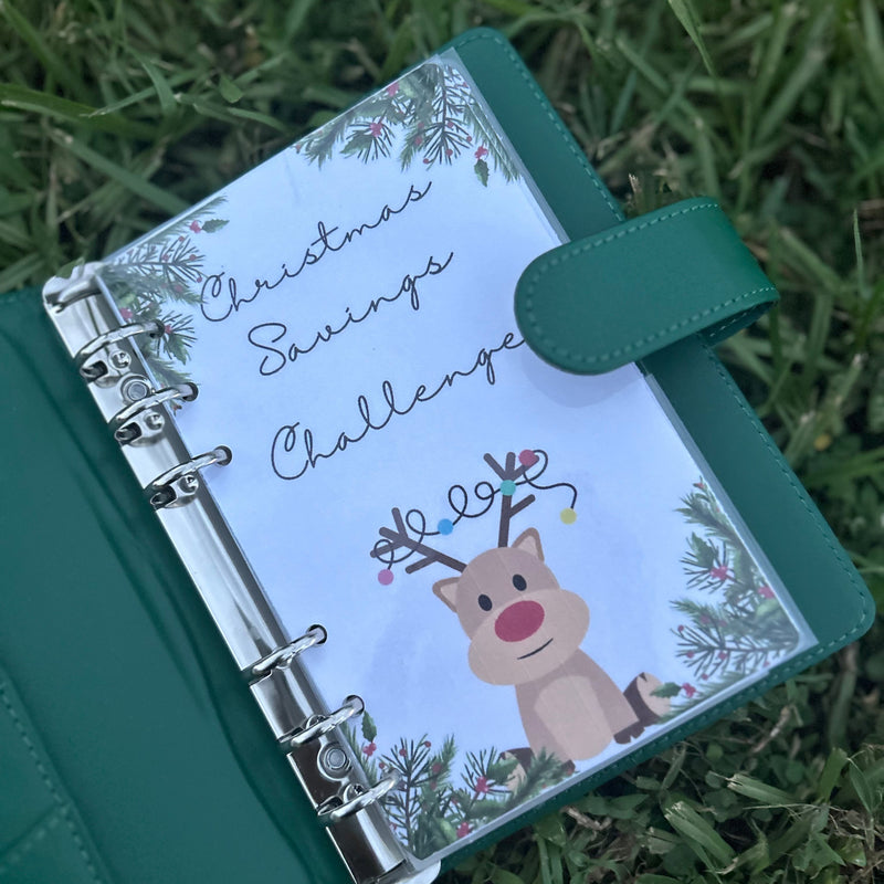 Green planner with a Christmas design on the cover, featuring a reindeer and text, placed on grass.
