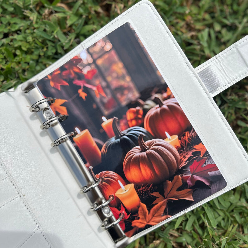 Open planner with a decorative page featuring pumpkins and candles on grass