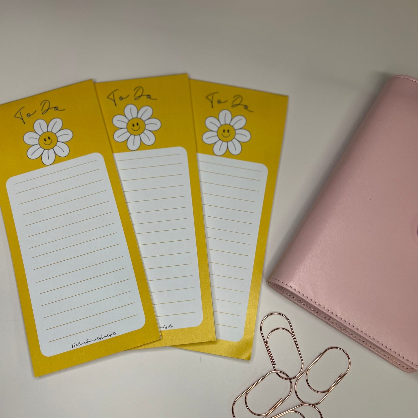Yellow notepads with daisy designs and a pink notebook on a white surface.