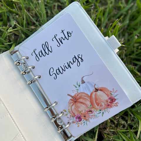 Small notebook with 'Fall Into Savings' cover on grass