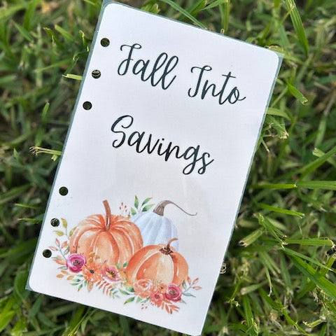 Notebook with 'Fall Into Savings' text and pumpkins on grass
