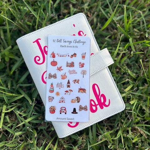 White planner with pink text and a sheet of stickers on grass