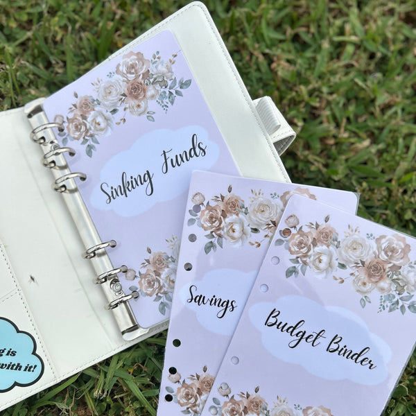 Floral-themed budget binder with 'Sinking Funds' and 'Savings' sections on a grass background.
