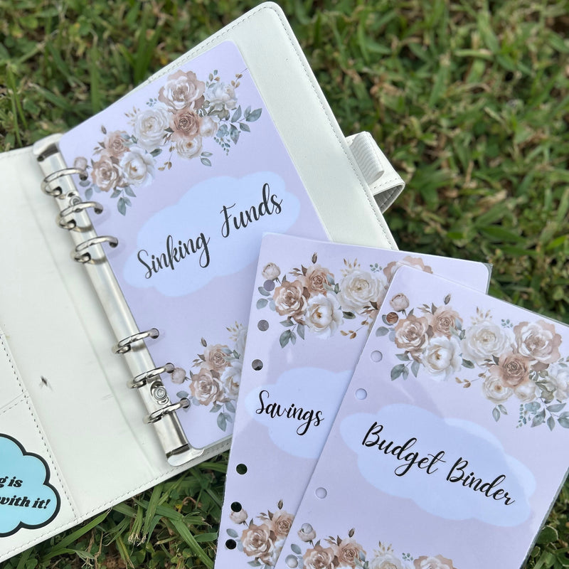 Floral-themed budget binder with 'Sinking Funds' and 'Savings' sections on a grass background.