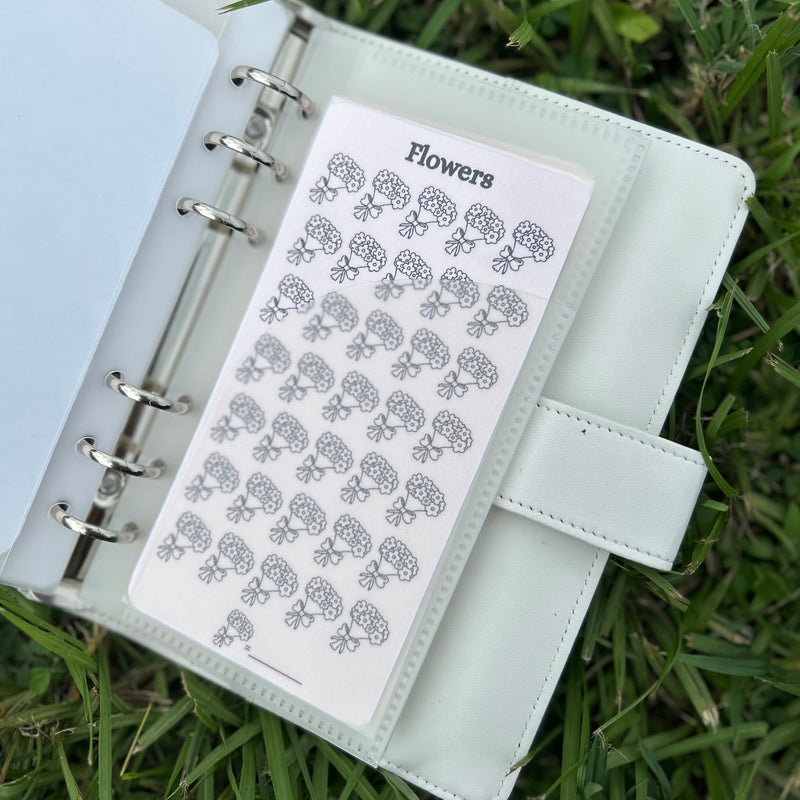 white planner with floral stickers on a grass background