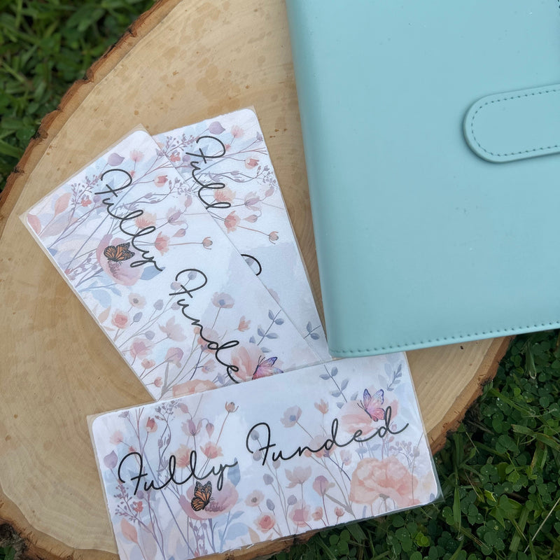 Light blue planner and three floral-themed cards on a wooden surface with grass in the background