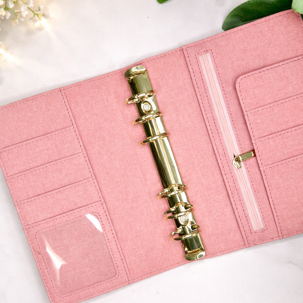 Pink planner with gold pen and decorative elements on a white surface