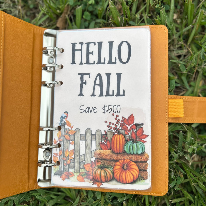 Open planner with 'Hello Fall' and pumpkin design on grass