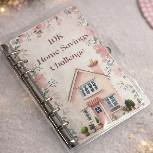 Planner with '10K Home Savings Challenge' on floral design cover, surrounded by decorative lights and flowers.