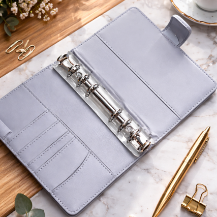 Gray planner with metal rings on a marble surface with flowers and a cup of coffee.
