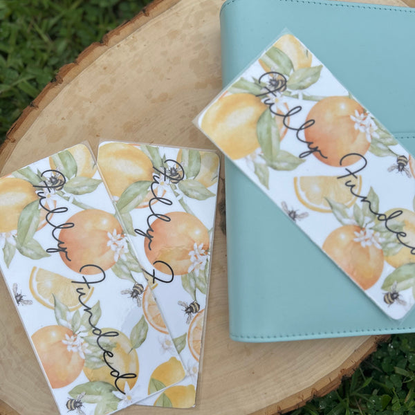 Two cards with lemon designs and a blue notebook on a wooden surface with grass in the background