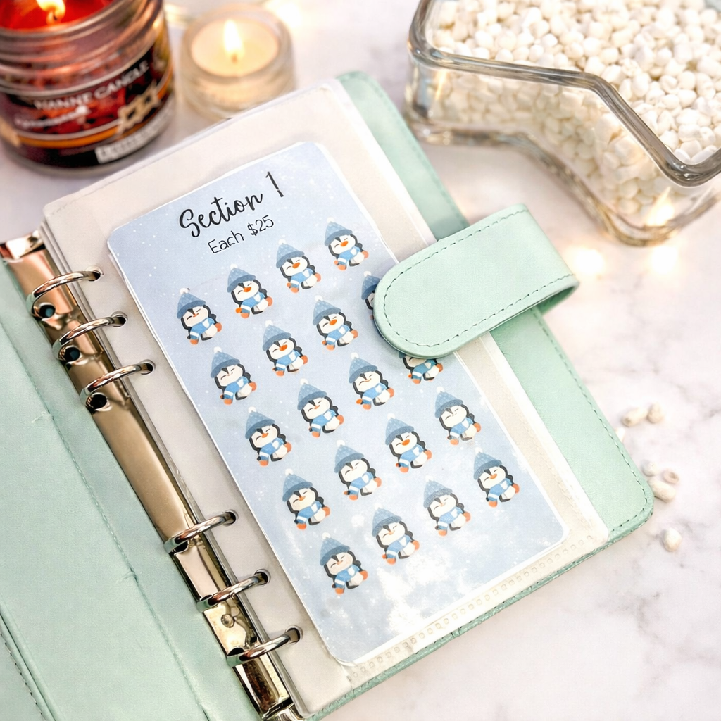 Planner with penguin stickers on a light surface with candles and a jar in the background