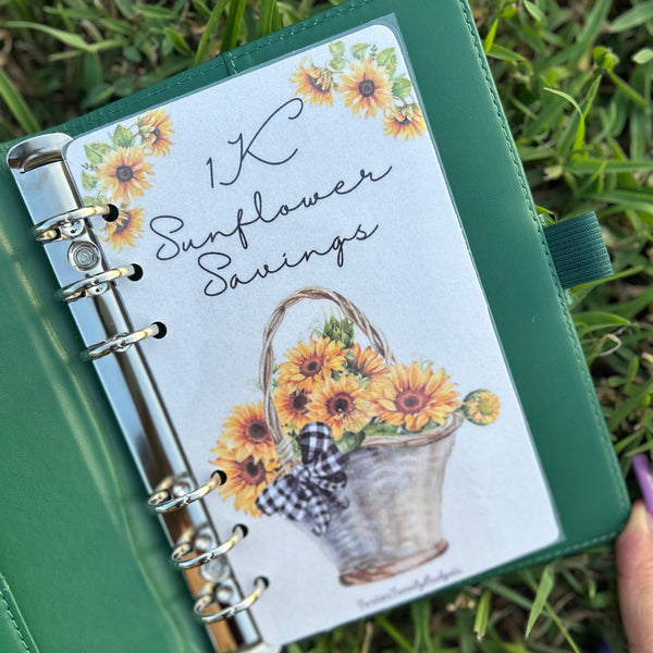 Green notebook with sunflower-themed cover held in grass