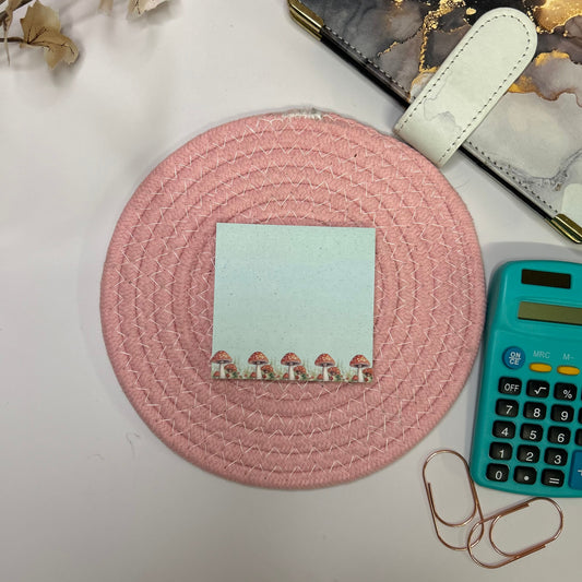 Round pink woven mat with a small card on a light surface, next to a calculator and phone.
